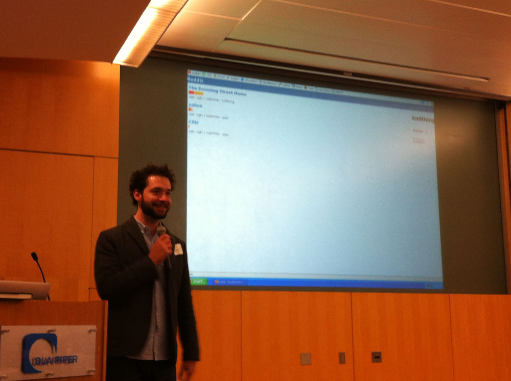 Alexis Ohanian speaking at Exec TechBreakfast in November. Behind him on the screen: a screenshot of the earliest version of reddit.com.