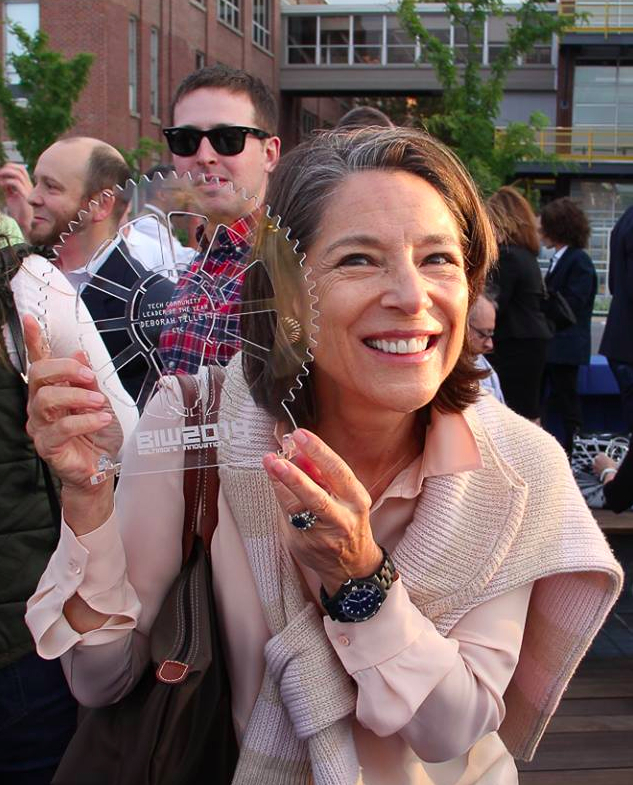 Deb Tillett smiles while holding glass award with red text