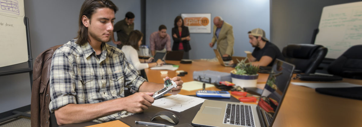 Jordan Burchfield works on a Spin In project for mTrigger while others (including Amy Lalime and Cyndi McLaughlin) work in the background.