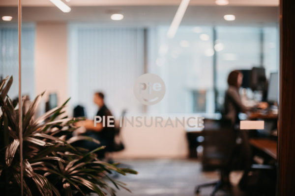 A glass door with the Pie Insurance logo. Employees are out of focus in the background.