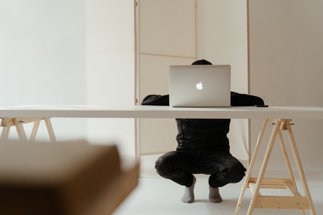 Man squatting at a laptop on a table
