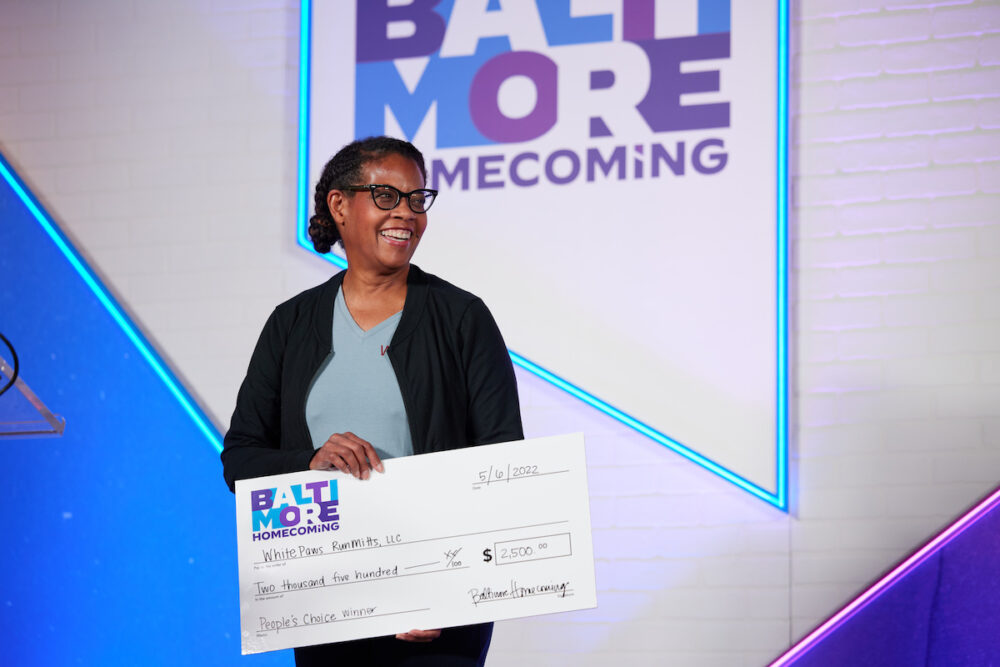 Susan Clayton in black sweater and blue shirt holding white novelty check with purple and blue text.