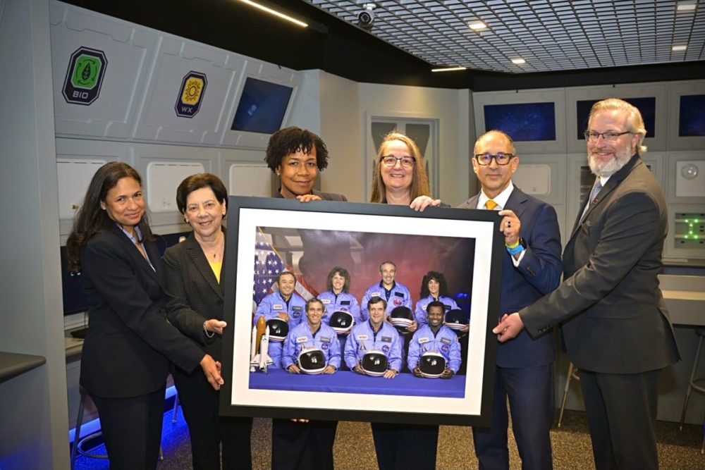 Challenger Center officials hold up a photo of the Challenger space crew.