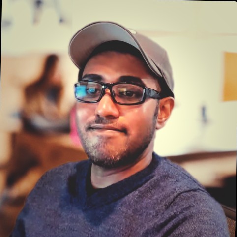 Noel Victor wearing glasses and a hat in front of a blurry background