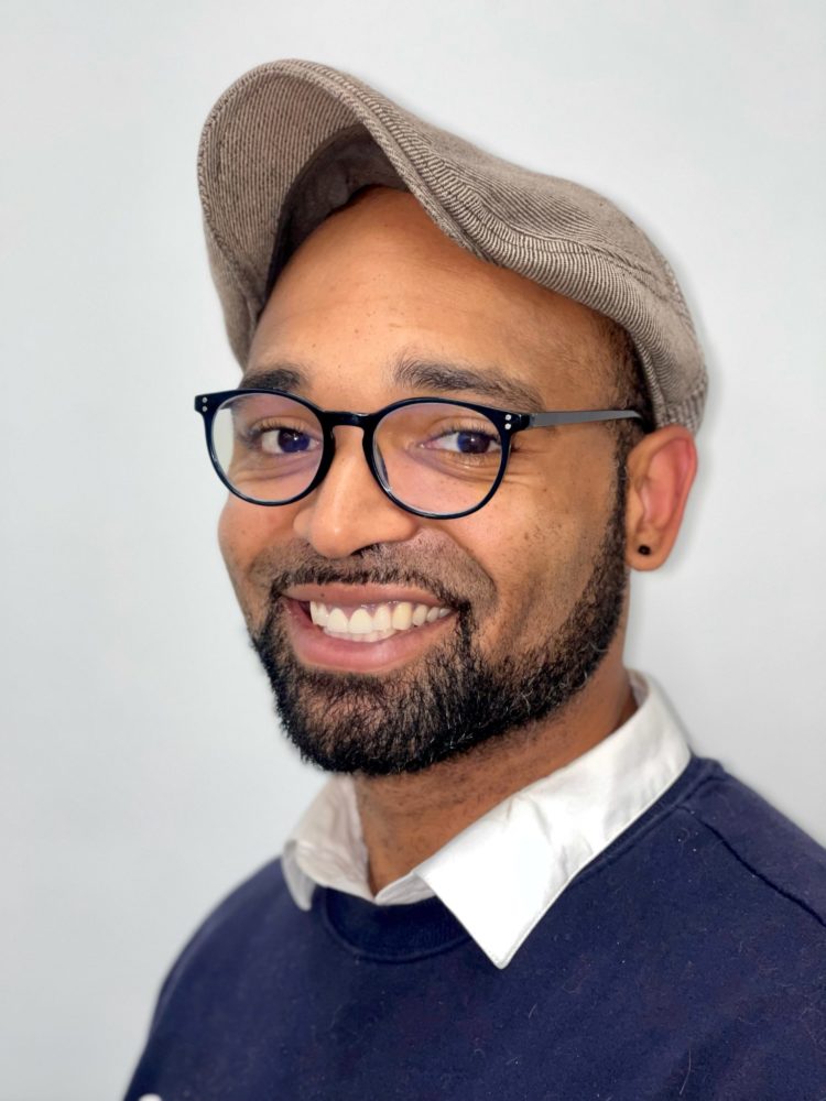 Brandon Washington wearing a hat and glasses with a grey background