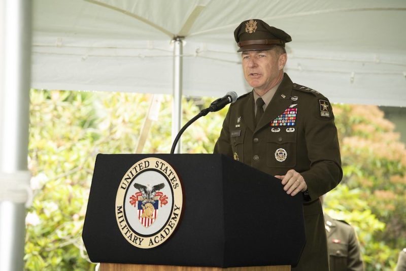 Man in brown military uniform speaks at podium with military insignia