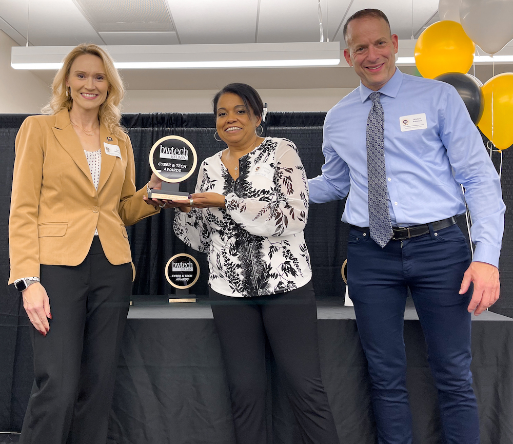 Three people pose with black and white award statue in front of black curtains and white ceiling