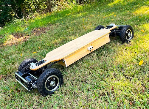 brown electric skateboard with black wheels and motor on green grass