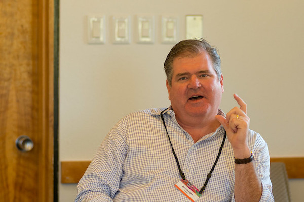 Man in light blue dress shirt smiles behind black nametag