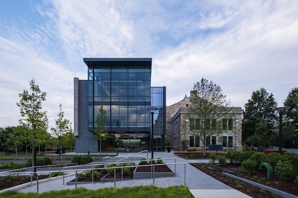 Blue glass and brown stone buildings near grey walkway before blue and white sky