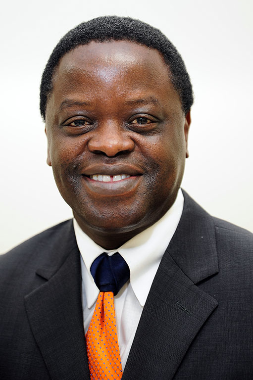 Man smiles in charcoal suit with navy and orange tie and white shirt.