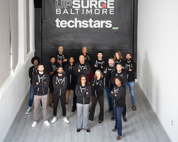 People in black hoodies pose before black wall reading "UPSURGE BALTIMORE" and "techstars" in white