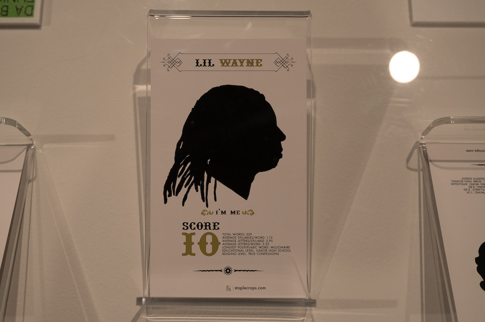 Silhouette of Lil Wayne near black and gold text with featuring his "I'm Me" lyrics on off-white wall.