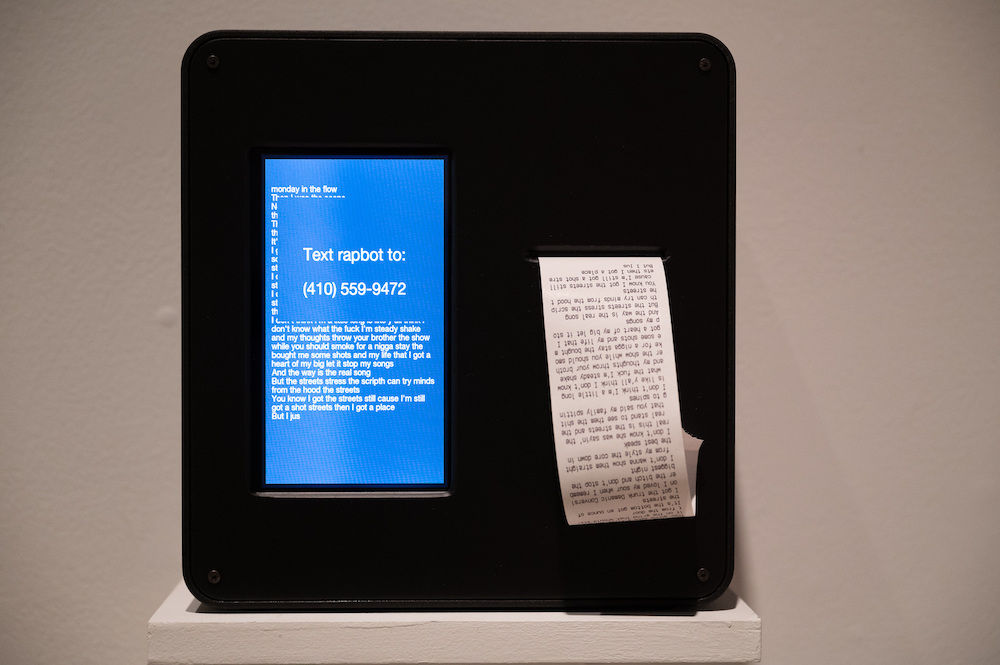 Black box with blue screen and white text next to white paper with black text, both presenting rap lyrics