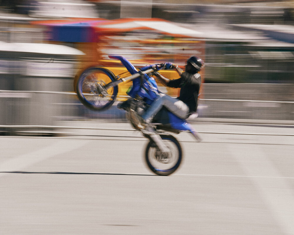 Person in black and grey on blue dirt bike in front of blurry background