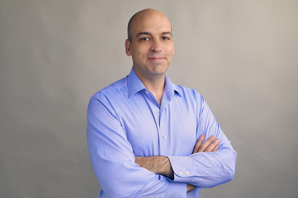 Sebastian Seiguer in light blue dress shirt with arms folded in front of grey-beige background.