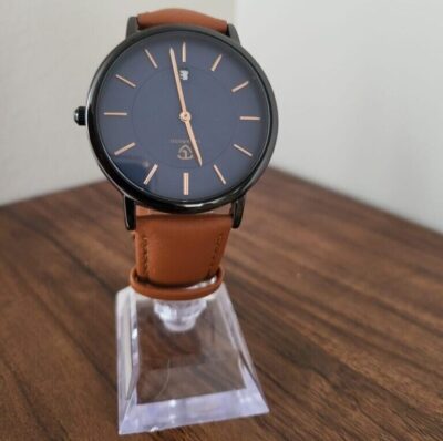 An analog wristwatch with a black dial and a tan leather strap displayed on a clear stand.