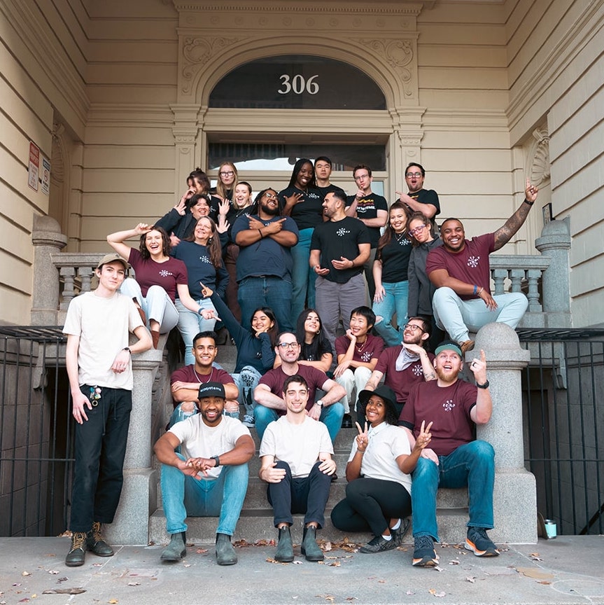 About two dozen members of the EcoMap Technologies team pose on the stairs of a beige building. They are wearing white, maroon and black T-shirts with the company logo.