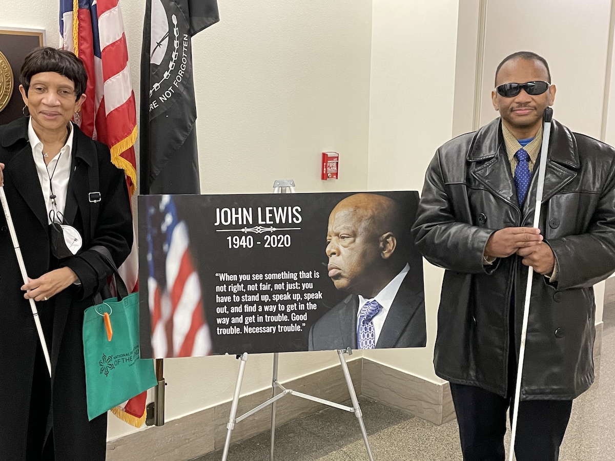 Two people stand and smile beside a poster board with Rep. Lewis' face.