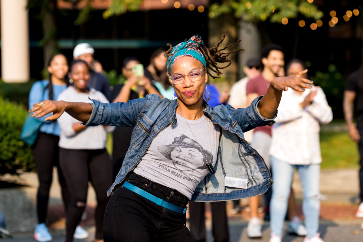 Woman dancing in blue denim jacket and grey shirt in front of crowd