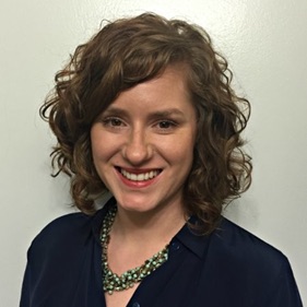 Maddy stokes in black shirt with green necklace before grey wall.