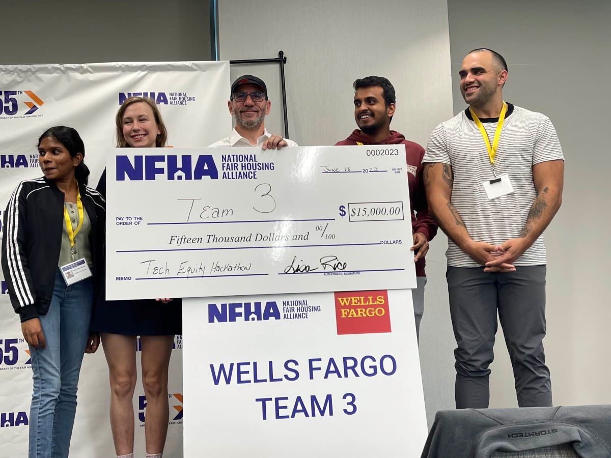 Four people stand holding a check for $15,000. A sign reads Wells Fargo Team 3. 