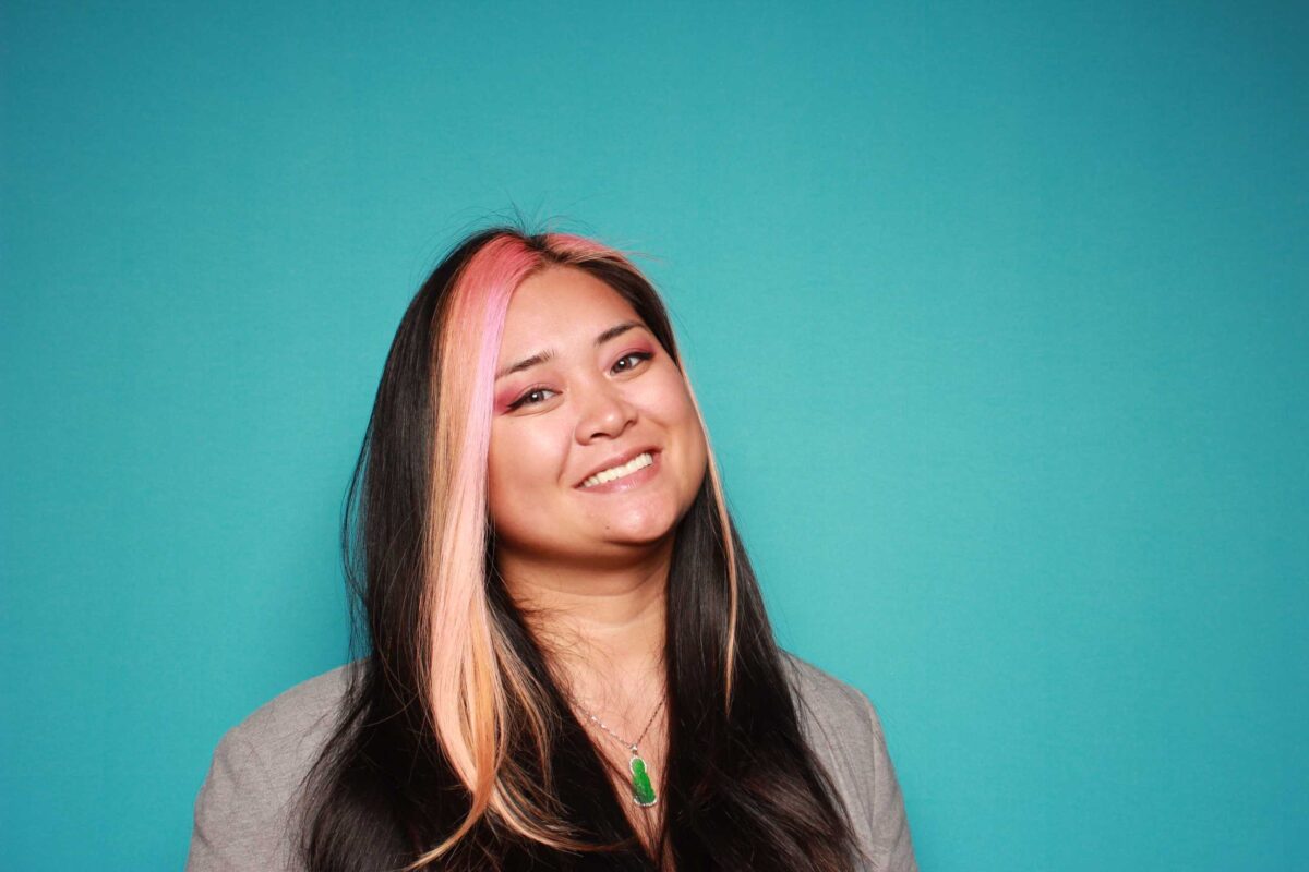 A headshot of Chrystina, who stands before a teal background.