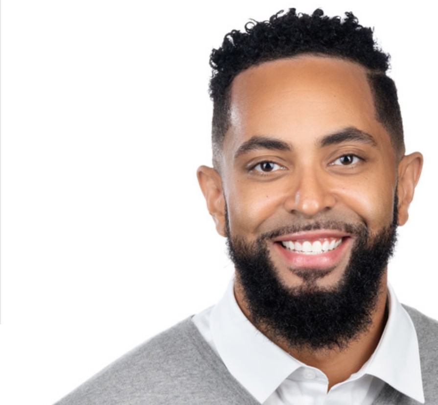 A headshot of Gerren Price, who wears a gray sweater and stands in front of a white background. 