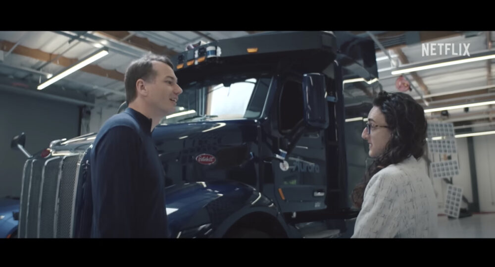 A man and woman speak while standing before a self-driving truck.