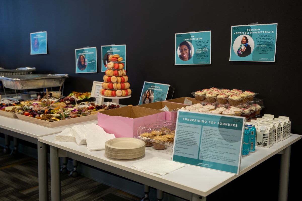 A display table with macaroons and other treats and teal printouts featuring vendor stories.