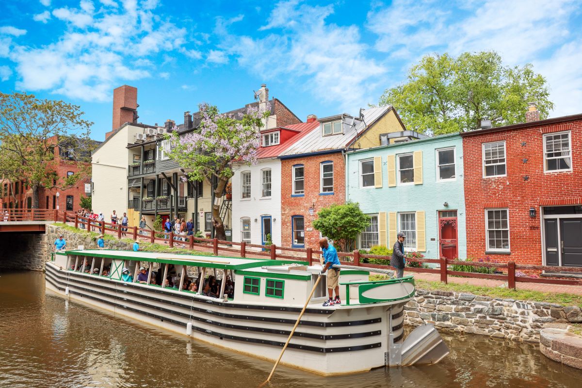 A view of colorful rowhouses along the canal. A canal boat stands in front. 