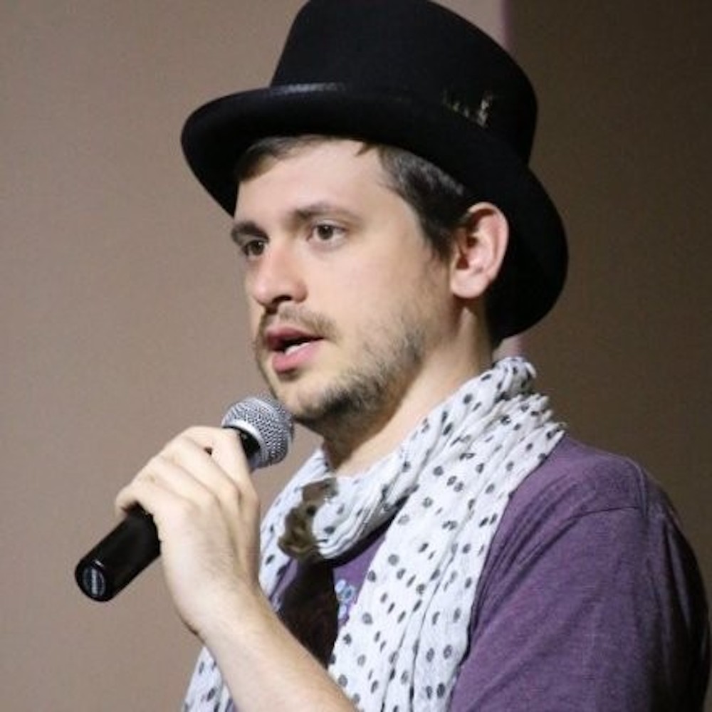 A man in a hat and scarf speaking into a microphone.