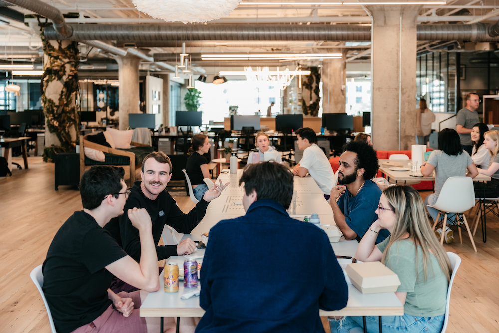 Photo of a group of Perpay employees sitting and conversing around a table in the kitchen area of their office.