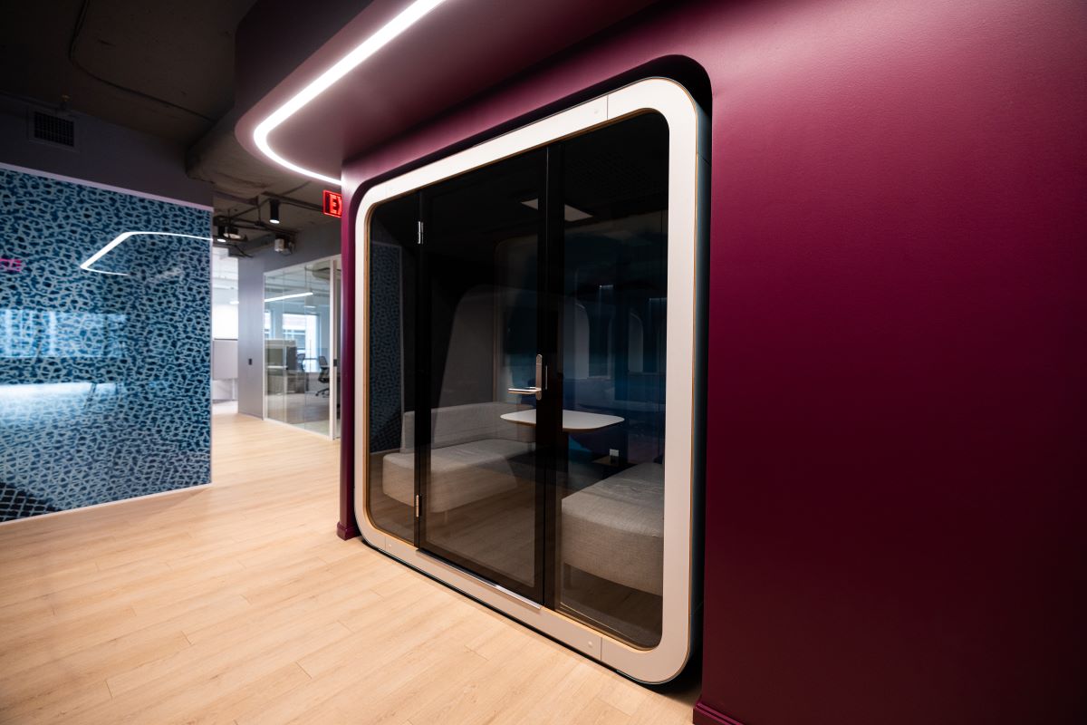 A dark glass phone booth sits in a maroon wall.