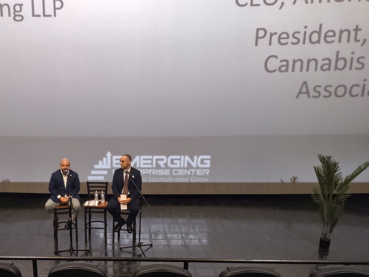 Peter Murphy and James Brobyn sitting in chairs in front of a big screen.