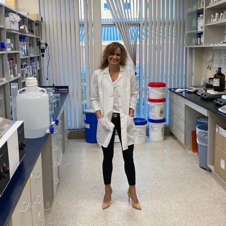 A woman in a lab coat standing in front of shelves.