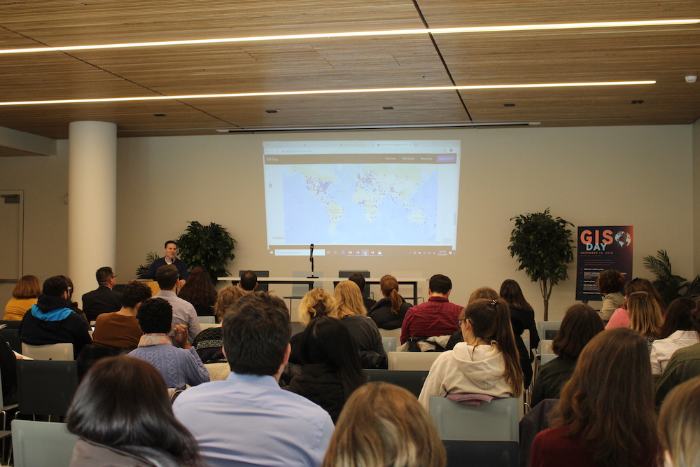 A group of people in a classroom watching a presentation for GIS Day featuring a map projected on the wall.