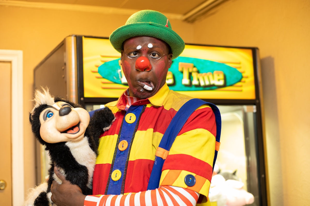 A clown holding a stuffed animal in front of a vending machine.