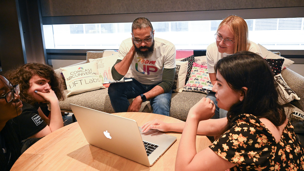 A group of people sitting around a table looking at a laptop.