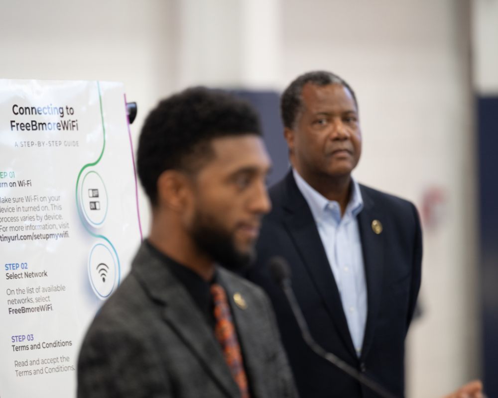 Brandon Scott and standing next to William Honablew Jr. at a podium.