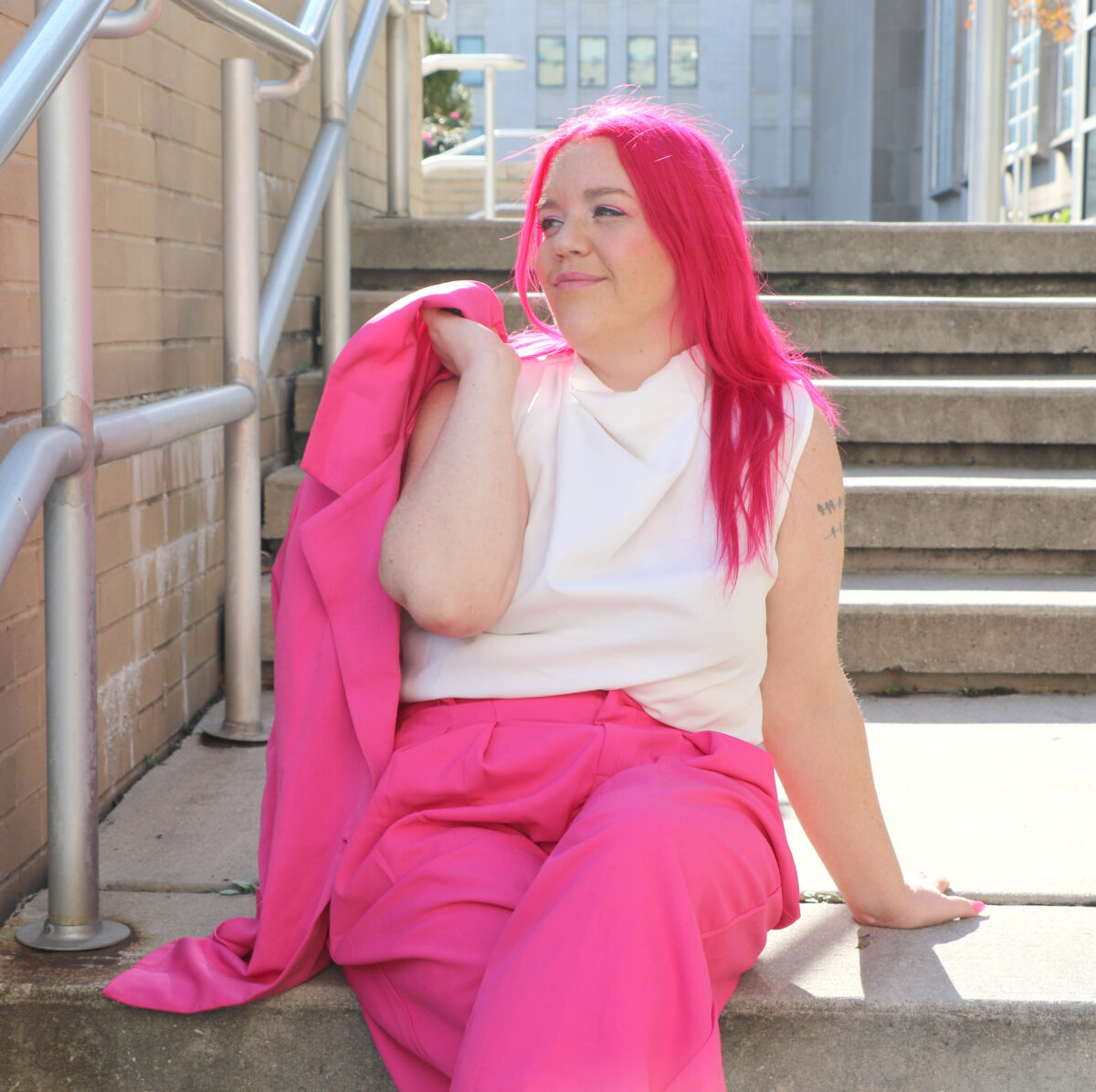 A woman with pink hair sitting on steps.