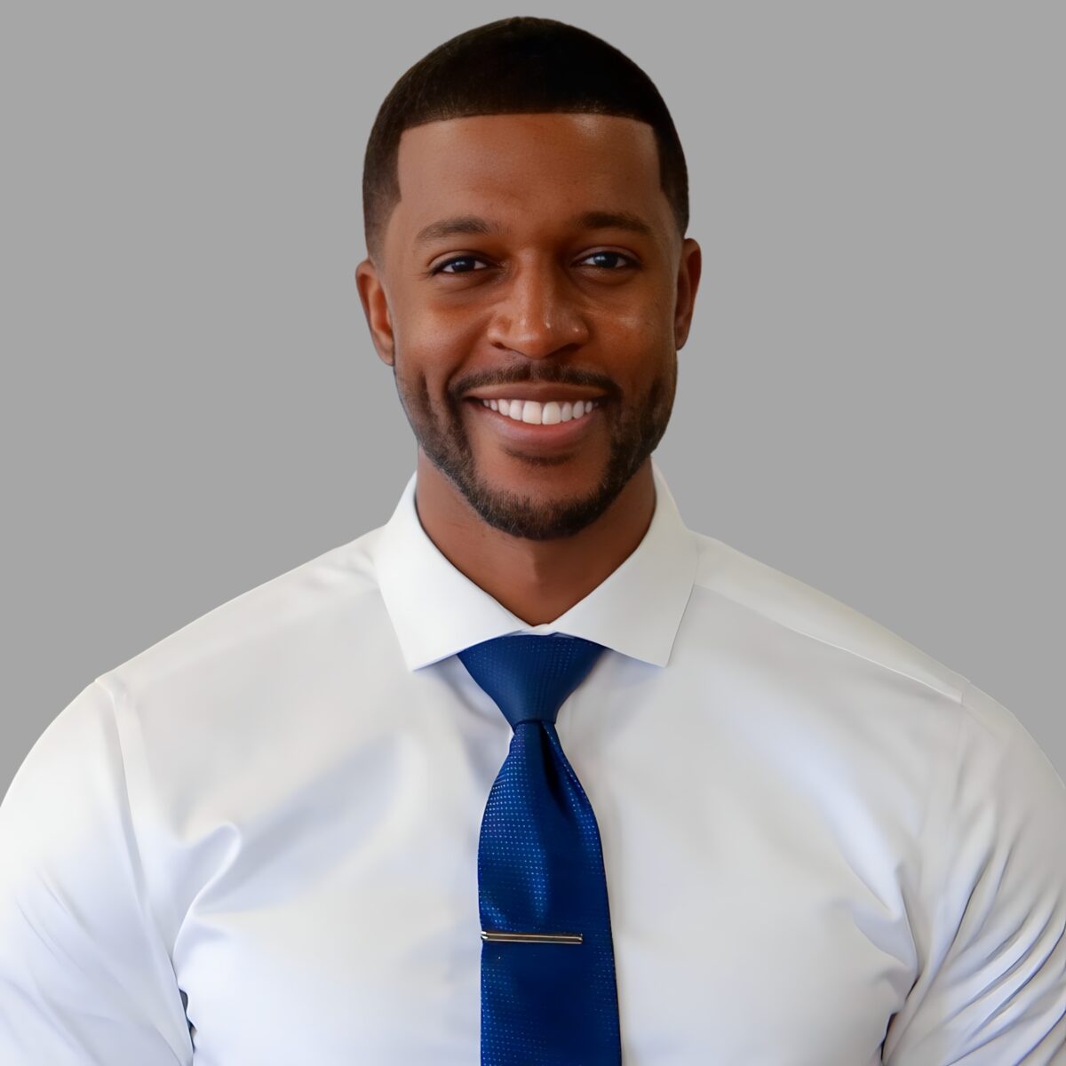 Joshua Reid in white shirt with blue tie before grey background.