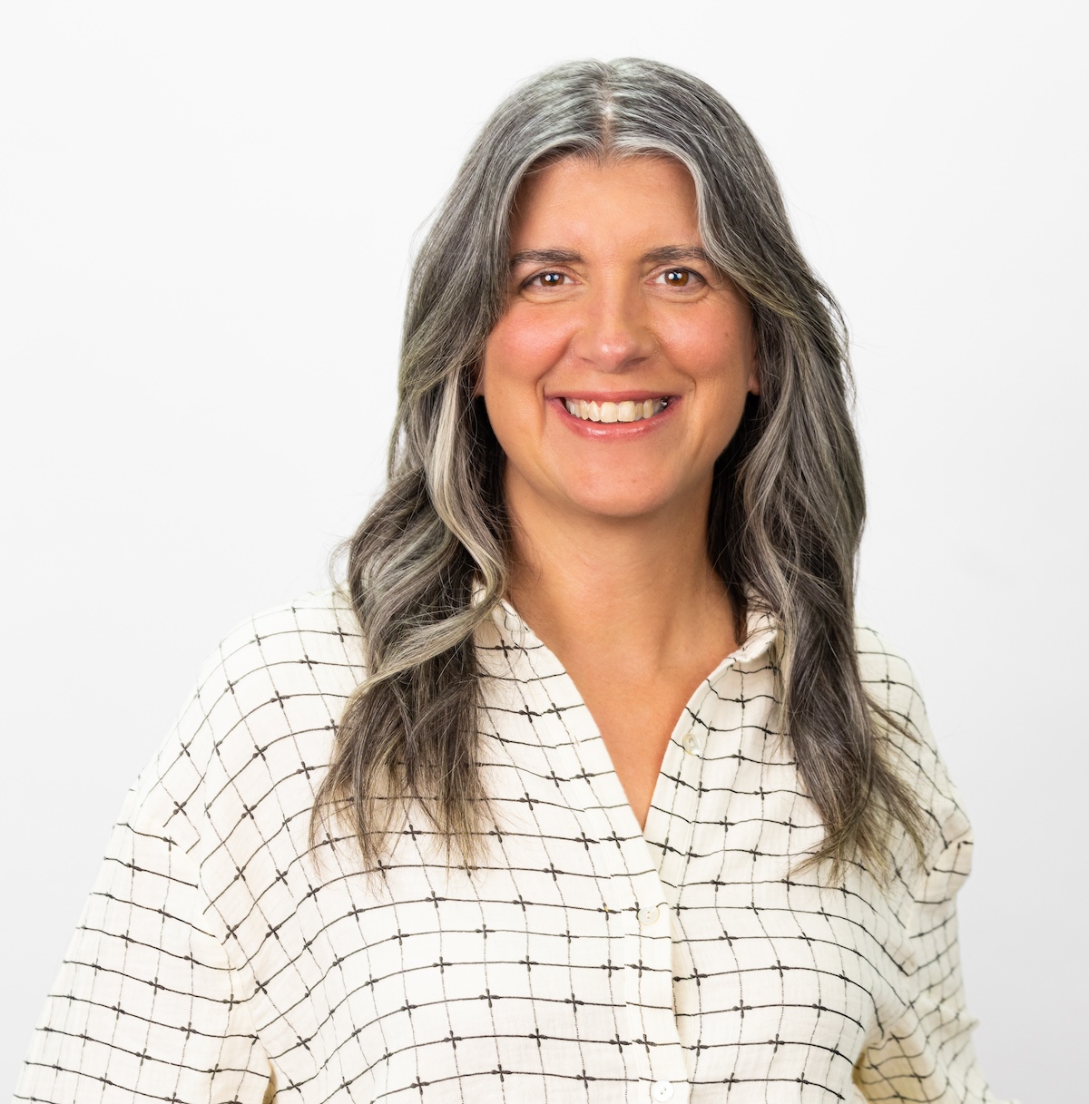 A woman in a cream-colored shirt smiles in front of a white background.