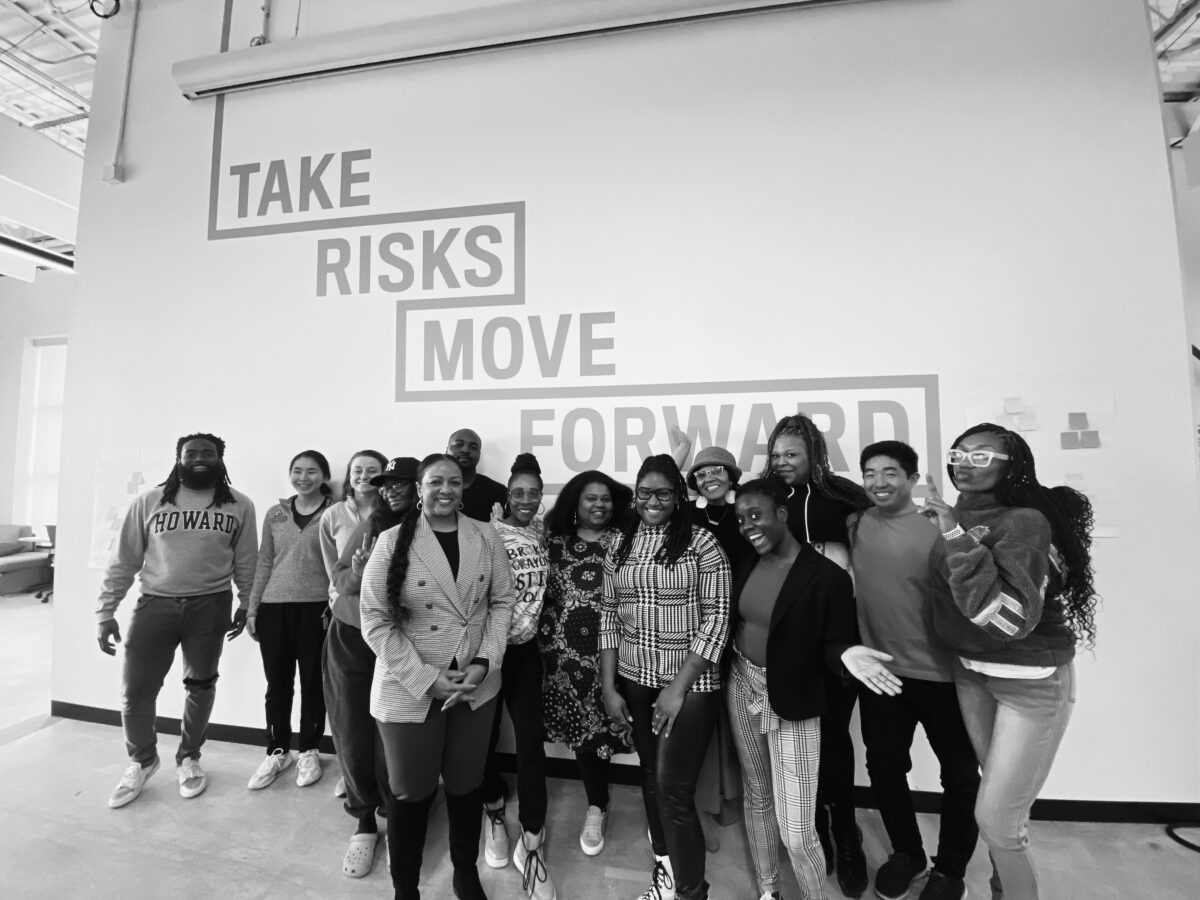 A group of Social Innovation Lab participants and LaKisha Greenwade standing in front of a wall that says "TAKE RISKS MOVE FORWARD."