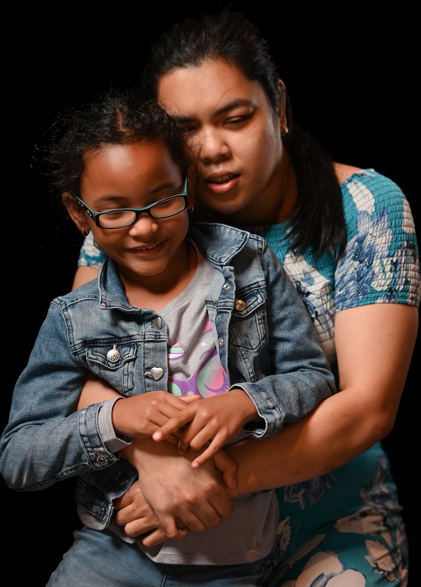 A mother and daughter hugging against a black background.