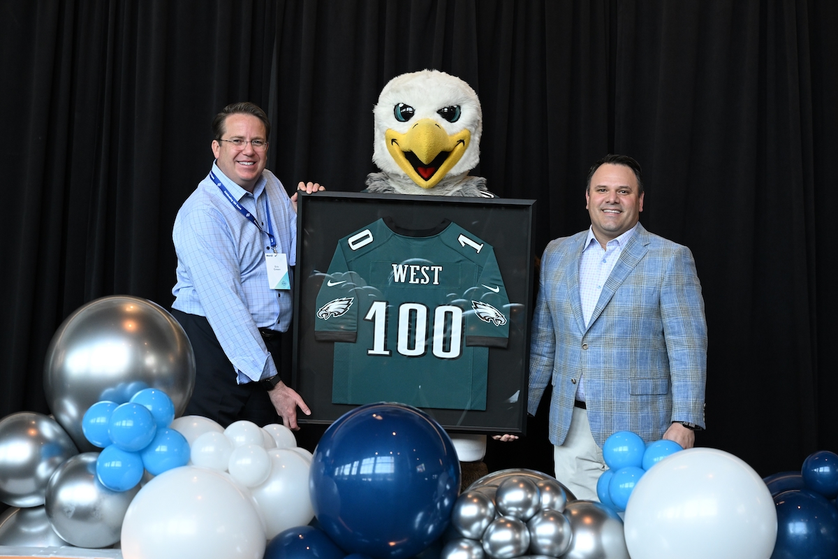 Two men standing next to a framed Eagles jersey held by Swoop, the Eagles mascot.