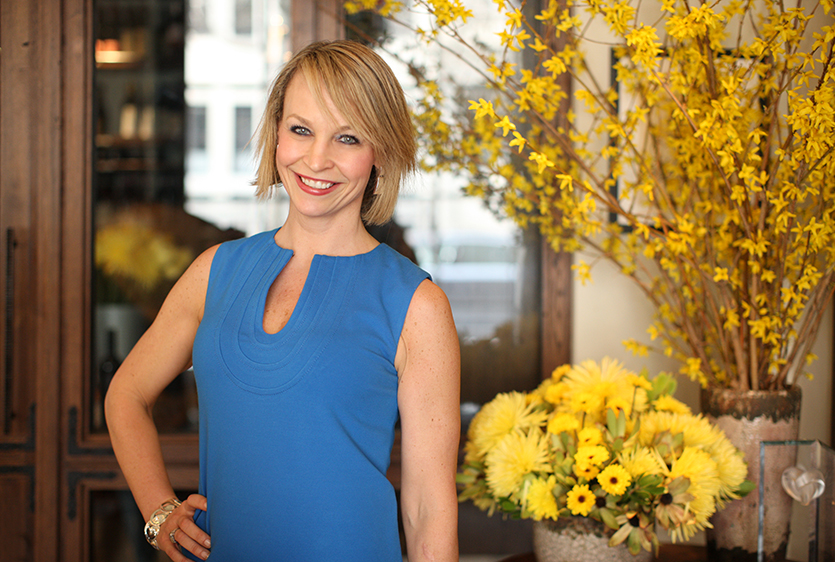 A woman in a blue dress standing in front of yellow flowers.