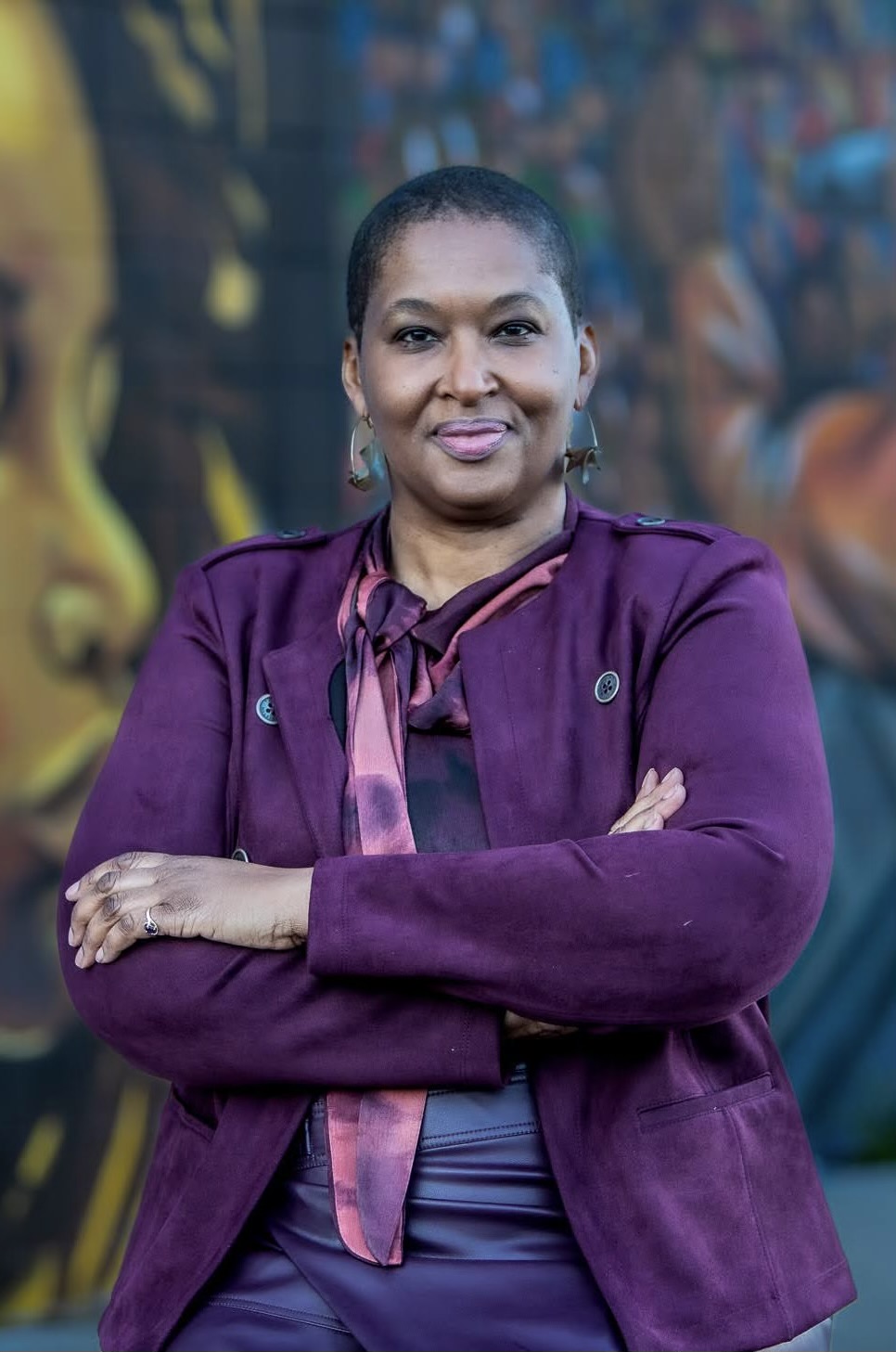 Rachel D. Graham in purple blazer and pink and purple scarf in front of mural.