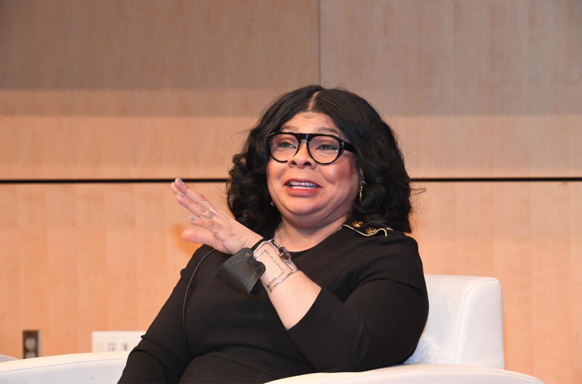 April Ryan in black shirt and glasses on white chair.