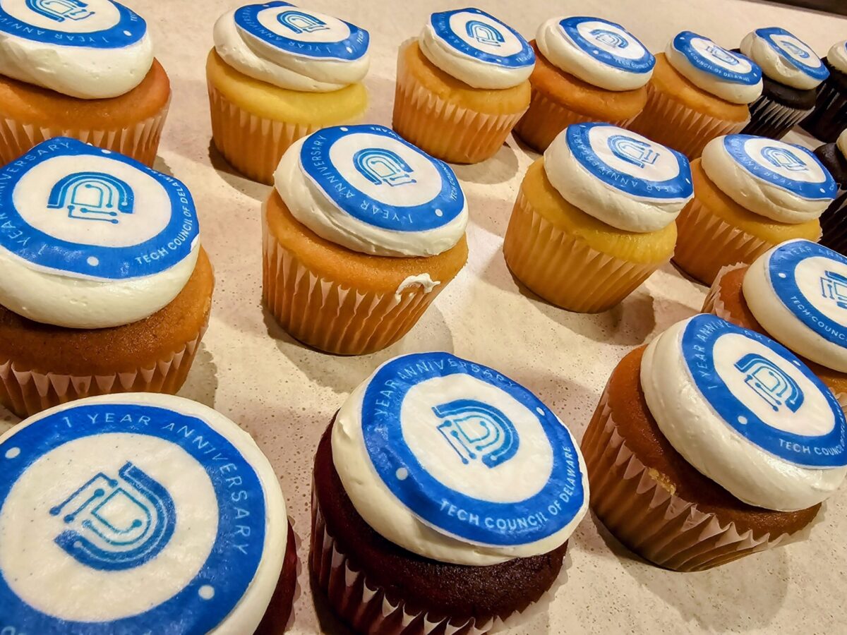 Assorted cupcakes with blue and white frosting, featuring logos to celebrate a tech council's one-year anniversary.